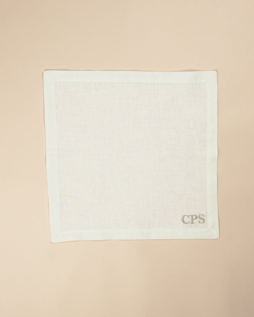 Plain white square napkin with beige embroidered initials on the bottom right corner