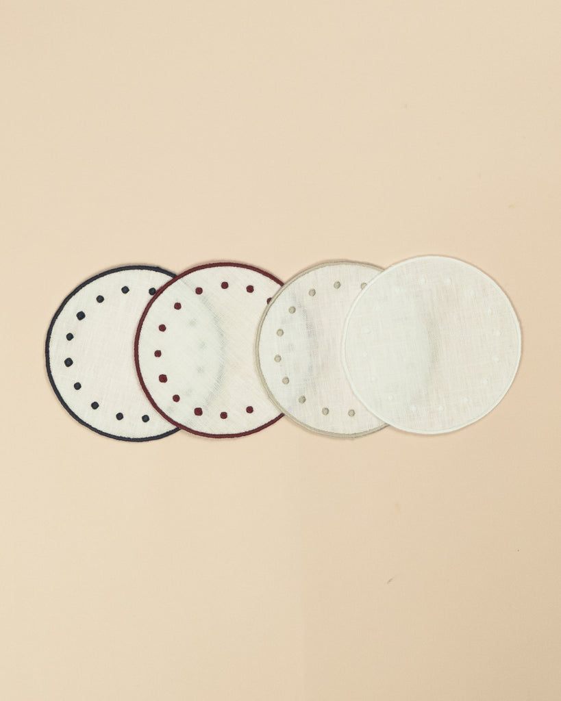 Set of four round side plates, all in white but with blue, bordeaux, beige and white colours on the embroidered edge and on the embroidered dots along the edge
