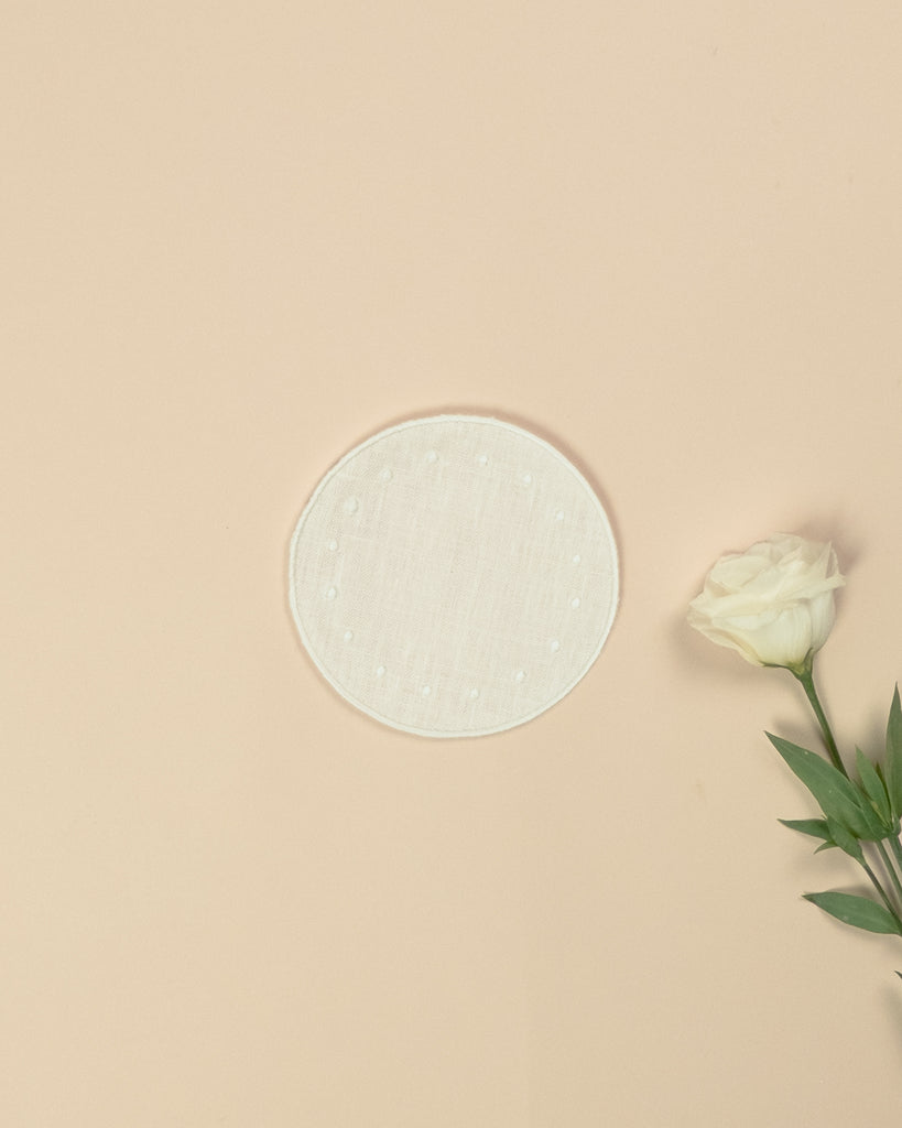 White round side plate with embroidered white borders and white dots, next to a white rose