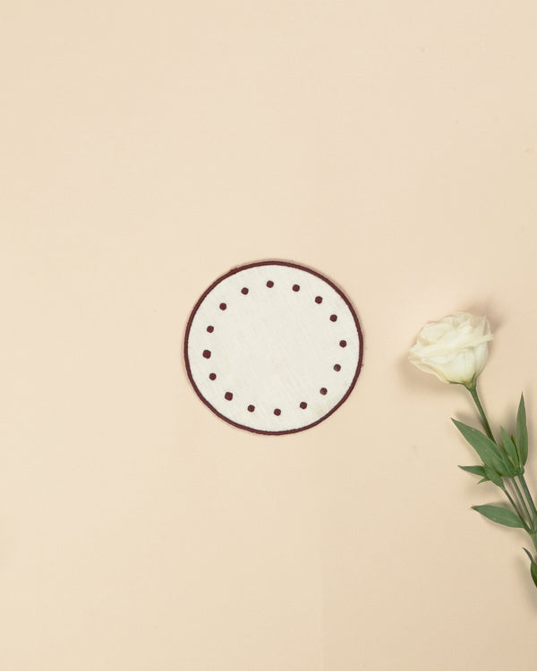 White round side plate with embroidered bordeaux borders and bordeaux dots along the edge, next to a white rose