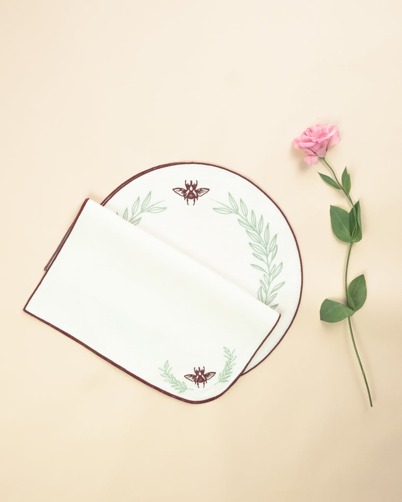Set of napkin and placemat, both in white, with embroidered bordeaux borders, an embroidered bordeaux scarab and embroidered green foliage