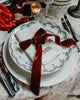 Festive Table Setting where a Napkin with embroidered initials, envolved in a red ribbon, stands on top of a ceramic plate