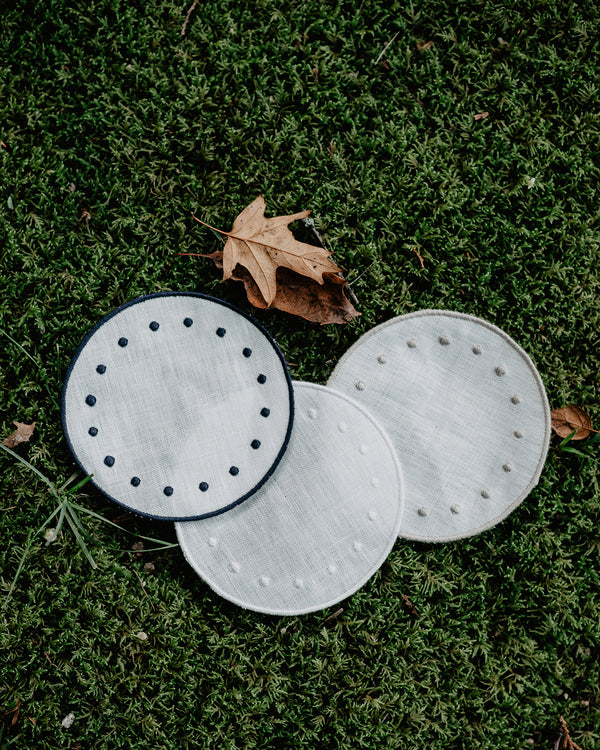 Set of three round side plates in a lawn, all in white but with blue, beige and white colours on the embroidered edge and on the embroidered dots along the edge